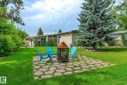 Expansive backyard featuring a central stone patio area with a fire pit, surrounded by lush green lawn - 10339 36A Avenue, Edmonton, AB - Outdoor With Backyard