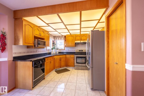 Kitchen featuring wood cabinetry, dark countertops, tiled backsplash, and stainless steel appliances - 5736 161 Avenue, Edmonton, AB - Indoor Photo Showing Kitchen