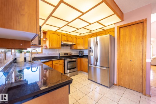 Kitchen featuring wood cabinetry, black countertops, stainless steel appliances, and a tiled floor - 5736 161 Avenue, Edmonton, AB - Indoor Photo Showing Kitchen