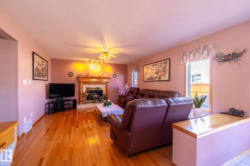 Living area featuring wood-finish flooring, a built-in fireplace with a stone surround and wood mantel, a ceiling fan with integrated lighting, and multiple windows - 5736 161 Avenue, Edmonton, AB - Indoor Photo Showing Living Room With Fireplace