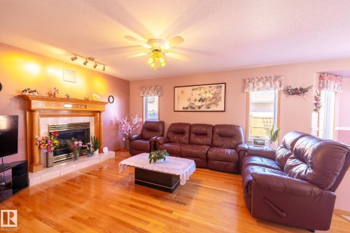 Living area featuring wood-finish flooring, a wood-surround fireplace with tile hearth, track lighting, and a ceiling fan with integrated lighting - 5736 161 Avenue, Edmonton, AB - Indoor Photo Showing Living Room With Fireplace