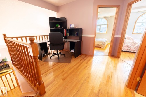 Upper-level open area featuring hardwood flooring, natural wood balustrade, and two arched doorways - 5736 161 Avenue, Edmonton, AB - Indoor Photo Showing Office
