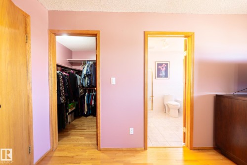 Light wood-finish flooring extending into a walk-in closet with built-in shelving, complemented by a nearby full bathroom featuring tiled flooring and a toilet - 5736 161 Avenue, Edmonton, AB - Indoor Photo Showing Other Room