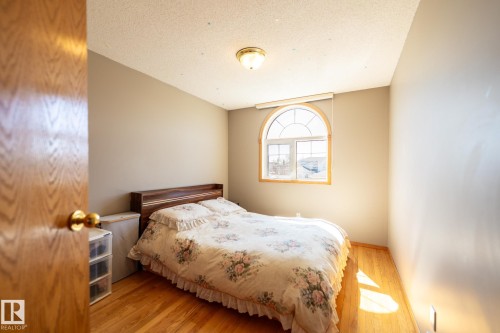 Bedroom featuring wood-finish flooring, an arched window with wood trim, neutral wall paint, a textured ceiling, and a flush-mount ceiling light fixture - 5736 161 Avenue, Edmonton, AB - Indoor Photo Showing Bedroom