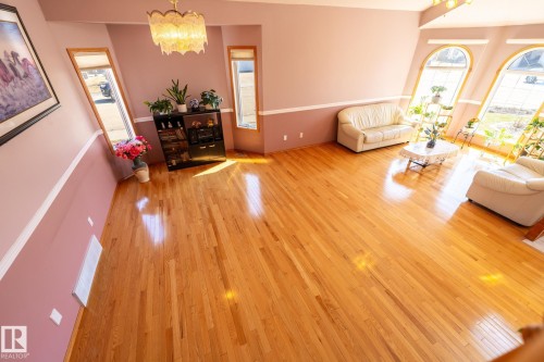 Expansive interior with lustrous wood-finish flooring, a contemporary chandelier, multiple arched windows, and a two-tone wall finish with chair rail molding - 5736 161 Avenue, Edmonton, AB - Indoor Photo Showing Living Room