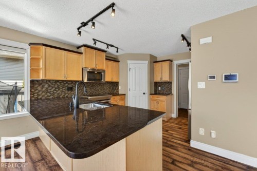 Kitchen featuring wood-finish flooring, light wood cabinetry, dark stone countertops, a mosaic tile backsplash, and stainless steel appliances - 10 Erickson Close, St. Albert, AB - Indoor Photo Showing Kitchen With Double Sink