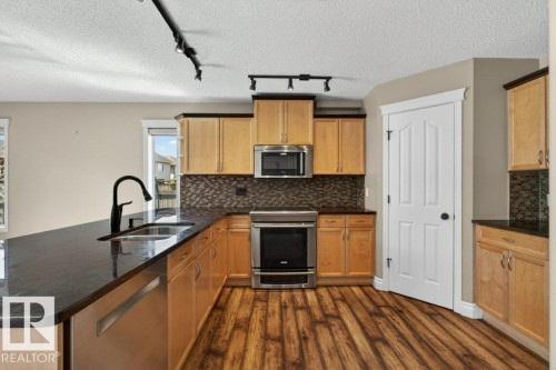 Spacious kitchen featuring light wood cabinetry, dark countertops, wood-finish flooring, stainless steel appliances, and a tiled backsplash - 10 Erickson Close, St. Albert, AB - Indoor Photo Showing Kitchen With Double Sink