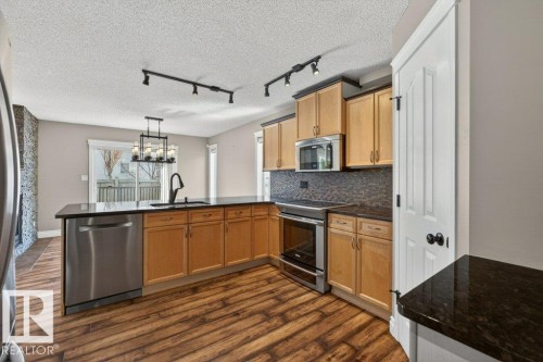 Kitchen featuring wood-finish flooring, dark granite countertops, stainless steel appliances, light wood cabinetry, and a mosaic tile backsplash - 10 Erickson Close, St. Albert, AB - Indoor Photo Showing Kitchen With Stainless Steel Kitchen