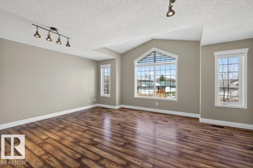 Spacious room featuring vaulted ceilings, wood-finish flooring, a large arched window, multiple casement windows, and track lighting - 10 Erickson Close, St. Albert, AB - Indoor Photo Showing Other Room