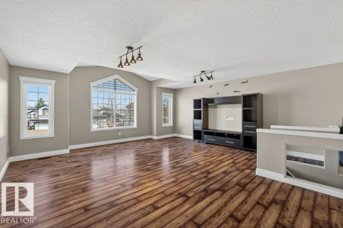 Spacious living area featuring wood-finish flooring, a vaulted ceiling, and multiple large windows including a prominent arched window - 10 Erickson Close, St. Albert, AB - Indoor