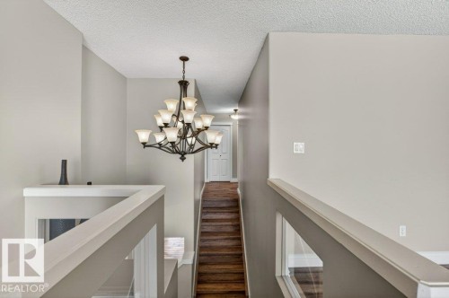 Multi-tiered chandelier illuminating a staircase with wood-finish treads and painted risers - 10 Erickson Close, St. Albert, AB - Indoor Photo Showing Other Room