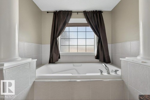 Built-in soaking tub with chrome fixtures, surrounded by light-toned tilework and decorative pillars - 10 Erickson Close, St. Albert, AB - Indoor Photo Showing Bathroom