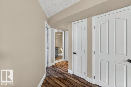 Hallway featuring wood-finish flooring, light neutral wall paint, white trim, and multiple panel doors with black hardware - 10 Erickson Close, St. Albert, AB - Indoor Photo Showing Other Room