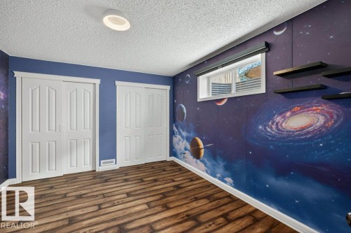 Wood-finish flooring complemented by a vibrant, celestial-themed accent wall - 10 Erickson Close, St. Albert, AB - Indoor Photo Showing Other Room