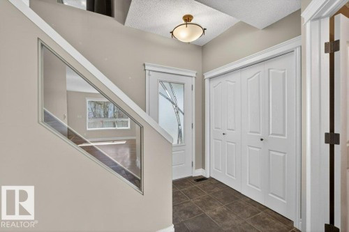 Entryway featuring tile flooring, a white bi-fold closet, a front door with decorative glass, a ceiling-mounted light fixture, and a glass-paneled stair railing - 10 Erickson Close, St. Albert, AB - Indoor Photo Showing Other Room
