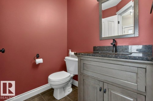 Powder room featuring a gray wood-finish vanity with a dark stone countertop, an undermount sink, and a framed mirror - 10 Erickson Close, St. Albert, AB - Indoor Photo Showing Bathroom