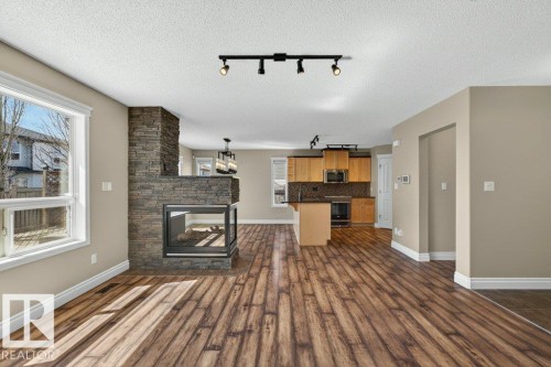 Living area featuring wood-finish flooring and a stone-clad fireplace with a glass enclosure - 10 Erickson Close, St. Albert, AB - Indoor Photo Showing Other Room With Fireplace