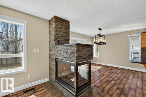 Central stacked stone fireplace with a three-sided glass enclosure - 10 Erickson Close, St. Albert, AB - Indoor With Fireplace