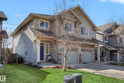 Two-story residence featuring light gray horizontal siding, stone accents, and a dark blue front door with an overhang - 2083 Chalmers Way, Edmonton, AB - Outdoor With Facade