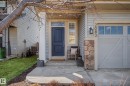 Front entry featuring a dark blue door with transom window, stone facade accents, an attached garage with upper window panels, and a concrete pathway - 2083 Chalmers Way, Edmonton, AB  - Outdoor 