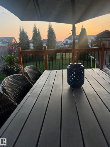 Expansive outdoor deck featuring wood railing with metal balusters, a large patio umbrella, and a fenced backyard with mature evergreen trees - 2083 Chalmers Way, Edmonton, AB - Outdoor With Exterior