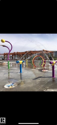 Splash pad featuring multiple colorful water features, ground-level sprayers, and a durable concrete surface - 2083 Chalmers Way, Edmonton, AB - 