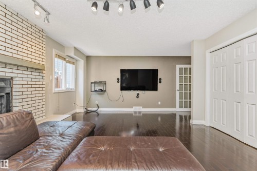 Living room featuring dark wood-finish flooring, a white brick fireplace with a wood mantle, and track lighting - 6016 177 Street, Edmonton, AB - Indoor Photo Showing Living Room With Fireplace