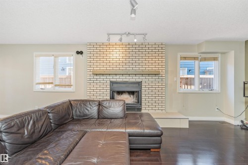 Living area featuring a brick fireplace with a wood mantel, a raised hearth, and dark wood-finish flooring - 6016 177 Street, Edmonton, AB - Indoor Photo Showing Living Room With Fireplace