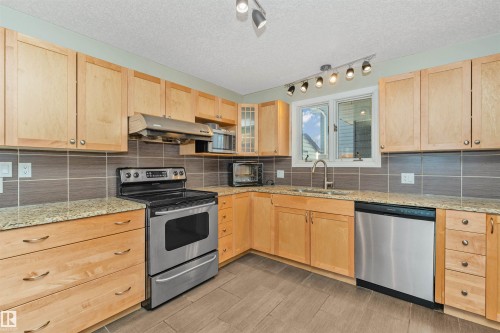 Kitchen featuring light wood cabinetry, granite countertops, a stainless steel range, a stainless steel dishwasher, and a tile backsplash - 6016 177 Street, Edmonton, AB - Indoor Photo Showing Kitchen With Stainless Steel Kitchen