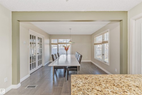 Dining area featuring wood-finish flooring, a contemporary pendant light fixture, and two large windows with blinds - 6016 177 Street, Edmonton, AB - Indoor Photo Showing Dining Room