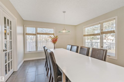 Spacious room featuring multiple windows with blinds, a sleek modern chandelier, and wood-finish tile flooring - 6016 177 Street, Edmonton, AB - Indoor Photo Showing Dining Room