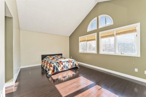 Spacious room featuring vaulted ceilings, a prominent arched window, two rectangular windows with blinds, and dark wood-finish flooring - 6016 177 Street, Edmonton, AB - Indoor Photo Showing Bedroom
