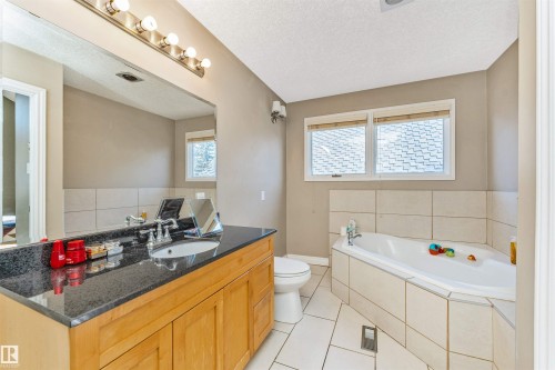 Spacious bathroom featuring a built-in corner bathtub, a light wood-finish vanity with a dark countertop, an integrated sink, and a large wall-mounted mirror - 6016 177 Street, Edmonton, AB - Indoor Photo Showing Bathroom