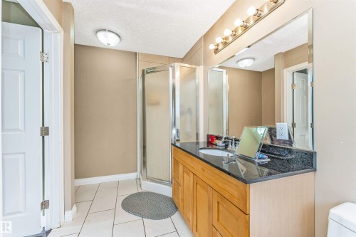 Bathroom featuring a wood-finish vanity with a dark countertop, integrated sink, and an expansive mirror - 6016 177 Street, Edmonton, AB - Indoor Photo Showing Bathroom