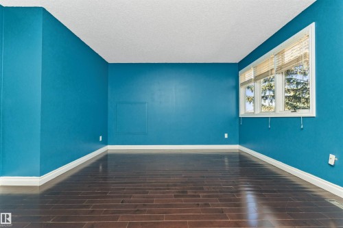 Spacious room featuring rich wood-finish flooring, vibrant blue walls, and crisp white baseboards - 6016 177 Street, Edmonton, AB - Indoor Photo Showing Other Room