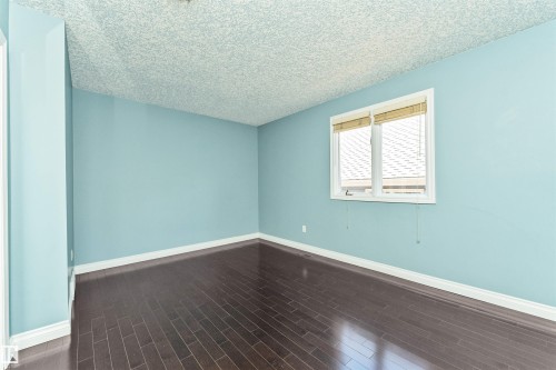 Room featuring wood-finish flooring, light blue painted walls, white baseboards, and a white-framed window with blinds - 6016 177 Street, Edmonton, AB - Indoor Photo Showing Other Room