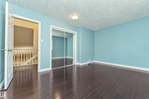 Spacious room featuring wood-finish flooring, light blue walls, and a popcorn ceiling with a flush-mount light fixture - 6016 177 Street, Edmonton, AB - Indoor Photo Showing Other Room