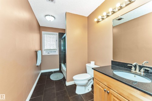 Bathroom featuring a wood-finish vanity with a dark countertop and undermount sink, a large wall-mounted mirror, a toilet, and dark tile flooring - 6016 177 Street, Edmonton, AB - Indoor Photo Showing Bathroom