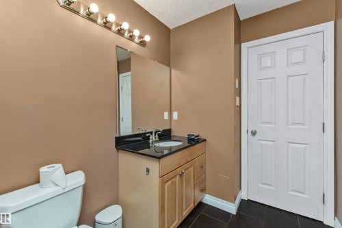 Bathroom featuring a wood-finish vanity with a built-in sink, a black countertop, and a large wall-mounted mirror - 6016 177 Street, Edmonton, AB - Indoor Photo Showing Bathroom