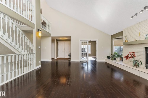 Expansive interior with rich wood-finish flooring, a two-story vaulted ceiling, white brick fireplace, and a prominent staircase with white balusters - 6016 177 Street, Edmonton, AB - Indoor Photo Showing Other Room