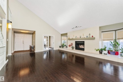 Spacious living area featuring high vaulted ceilings, rich wood-finish flooring, a white painted brick fireplace with hearth, double entry doors, and french doors - 6016 177 Street, Edmonton, AB - Indoor With Fireplace