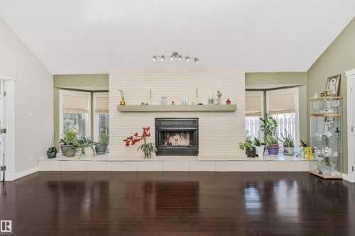 Spacious living area featuring dark wood-finish flooring, a white brick fireplace with a matching hearth, and a mantel shelf - 6016 177 Street, Edmonton, AB - Indoor With Fireplace
