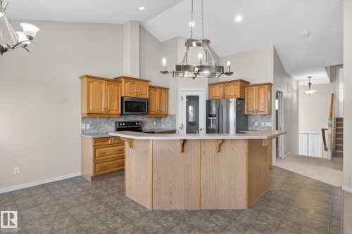 Kitchen featuring light wood cabinetry, stainless steel appliances, a tile backsplash, and an island with counter seating - 34 3003 34 Avenue, Edmonton, AB - Indoor Photo Showing Kitchen