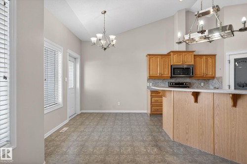 Kitchen area featuring wood cabinetry, stainless steel microwave, and a breakfast bar with a light countertop - 34 3003 34 Avenue, Edmonton, AB - Indoor Photo Showing Kitchen
