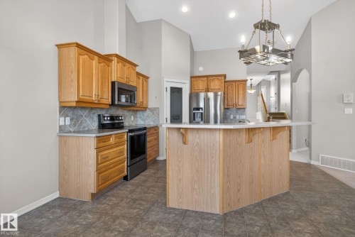 Kitchen featuring wood cabinetry, stainless steel appliances, a tiled backsplash, a central island with a breakfast bar, and tile flooring - 34 3003 34 Avenue, Edmonton, AB - Indoor Photo Showing Kitchen
