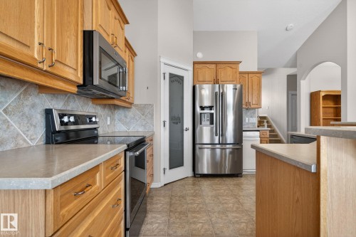 Kitchen featuring wood cabinetry, stainless steel appliances, a tiled backsplash, and light-toned countertops - 34 3003 34 Avenue, Edmonton, AB - Indoor Photo Showing Kitchen