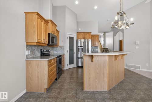 Kitchen featuring wood cabinetry, stone-look countertops, and a full suite of black and stainless steel appliances - 34 3003 34 Avenue, Edmonton, AB - Indoor Photo Showing Kitchen