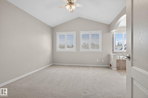 Vaulted ceiling room with two windows featuring white plantation shutters, neutral carpeting, and an arched entry to a tiled bathroom area with a built-in tub - 34 3003 34 Avenue, Edmonton, AB - Indoor Photo Showing Other Room