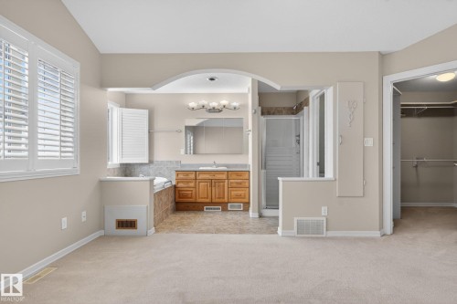 Carpeted room with a partial wall opening to a bathroom featuring a wood-finish vanity with a single sink and a mirrored medicine cabinet - 34 3003 34 Avenue, Edmonton, AB - Indoor