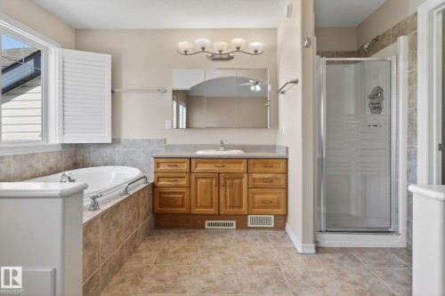 Bathroom featuring a built-in soaking tub with tile surround, a separate glass-enclosed shower, and a single vanity with wood cabinetry and a light-toned countertop - 34 3003 34 Avenue, Edmonton, AB - Indoor Photo Showing Bathroom